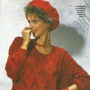 May include: A woman in a red beret, earrings, and a patterned knit sweater. The sweater has a textured design. The image also includes text in German.
