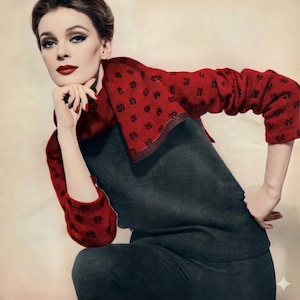 May include: A woman in a dark grey sweater and trousers, with a red sweater featuring a black floral pattern draped over her shoulders and arms. The woman has dark hair and red lipstick. The image has a vintage aesthetic.