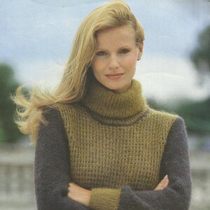 May include: A woman wearing a knitted turtleneck sweater. The sweater features a textured, olive green bodice and dark gray sleeves and collar. The woman has long, blonde hair.