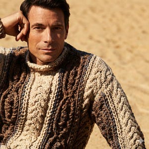 May include: A close-up of a cable-knit sweater in shades of brown and beige. The sweater has a high, ribbed collar and a textured pattern. The sleeves are long, and the overall design is warm and inviting.