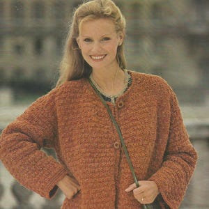 May include: A woman wearing a textured, rust-colored cardigan with three buttons. The cardigan has a round neckline and long sleeves. She is also wearing a necklace and a green strap bag.