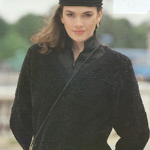 May include: A woman wearing a black knit hat and a black textured jacket with a zipper. She is also wearing a black top underneath the jacket and a small black purse with a gold clasp.