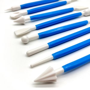 May include: A set of nine blue and white cake decorating tools with various shapes and sizes. The tools are made of plastic and have a white tip.