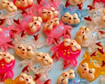 May include: Assortment of colorful resin deer charms with closed eyes and painted details. The charms are in various colors, including pink, blue, yellow, and white.