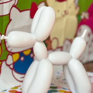 May include: White balloon animal sculpture in the shape of a dog. The sculpture is sitting on a colorful polka dot surface.