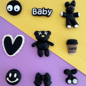 May include: A set of nine black and white iron-on patches featuring various designs, including a heart, a coffee cup, a teddy bear, a smiley face, a bow, and the word "Baby".