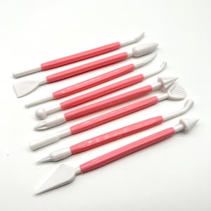 May include: Set of eight pink handled cake decorating tools with white plastic tips. The tips have various shapes for decorating cakes and pastries.