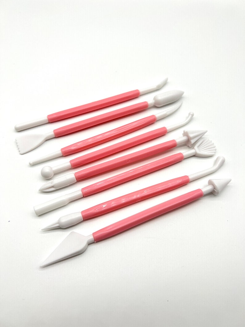 May include: Set of eight pink handled cake decorating tools with white plastic tips. The tips have various shapes for decorating cakes and pastries.