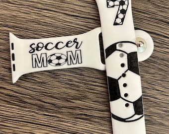 Puede incluir: Banda blanca para Apple Watch con un diseño de balón de fútbol negro y el texto "soccer mom" y el número "7" en la banda.