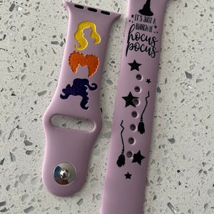 Puede incluir: Dos bandas de Apple Watch de silicona púrpura con diseños temáticos de Hocus Pocus en negro. Una banda presenta las siluetas de las hermanas Sanderson y la otra banda presenta estrellas, escobas y el texto "It's just a bunch of Hocus Pocus."