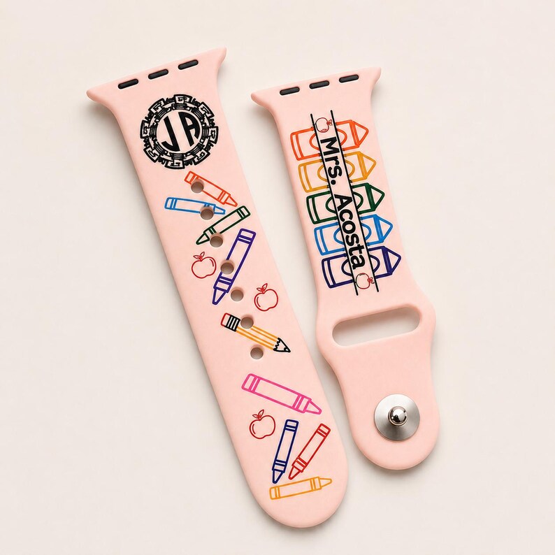 May include: A light pink silicone watch strap featuring a school-themed design with colourful crayon and apple illustrations. One side displays a circular monogram with the letters JA, while the other side features the text Mrs. Acosta.