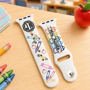May include: A white silicone watch strap featuring a colourful school-themed print with crayons, pencils, and apples. One side displays a circular monogram with the letters JP, while the other side features the text Mrs. Acosta printed vertically.