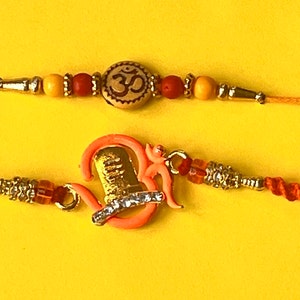 A Pair of Beautiful Shivling Om charm Rakhi and Om Beaded Rakhi with Complimentary Kumkum Chawal and handwritten Rakshabandhan Card.