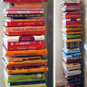 K&ouml;nnte beinhalten: Ein Stapel Kochb&uuml;cher mit bunten Umschl&auml;gen, darunter Titel wie "Simply Organic", "The Comfort Table II", "Joy Mixology" und "Taming the Flame".