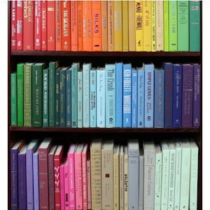 K&ouml;nnte beinhalten: Ein B&uuml;cherregal gef&uuml;llt mit bunten B&uuml;chern, sortiert nach Farbe von Rot bis Gr&uuml;n, Blau, Lila, Rosa und Hellblau. Die B&uuml;cher sind in Reihen in den Regalen angeordnet, wobei die R&uuml;cken nach au&szlig;en zeigen. Die B&uuml;cher sind alle unterschiedlich gro&szlig; und geformt und haben eine Vielzahl von Titeln und Autoren.