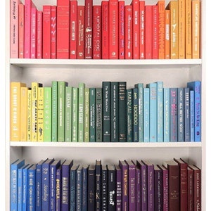 K&ouml;nnte beinhalten: Ein wei&szlig;es B&uuml;cherregal mit drei Regalbrettern, die mit bunten B&uuml;chern gef&uuml;llt sind. Die B&uuml;cher sind nach Farbe sortiert, beginnend mit Orange und Gelb im oberen Regal, dann Gr&uuml;n und Blau im mittleren Regal und schlie&szlig;lich Lila und Rot im unteren Regal.
