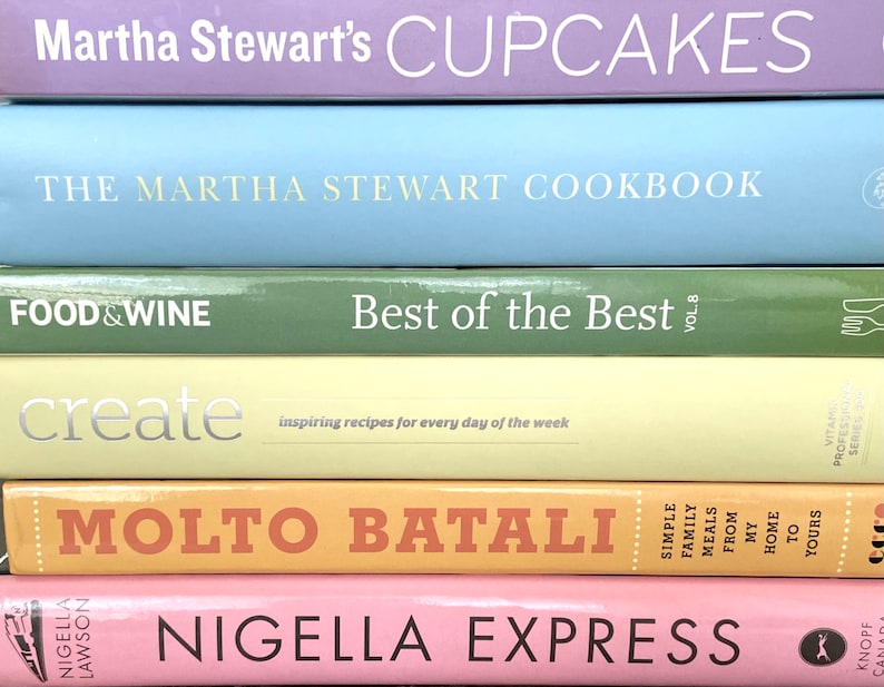 K&ouml;nnte beinhalten: Ein Stapel von sechs Kochb&uuml;chern mit bunten Umschl&auml;gen. Das oberste Buch ist lila und sagt "Martha Stewart's Cupcakes". Das zweite Buch ist hellblau und sagt "The Martha Stewart Cookbook". Das dritte Buch ist gr&uuml;n und sagt "Food & Wine Best of the Best Vol. 8". Das vierte Buch ist gelb und sagt "create inspiring recipes for every day of the week". Das f&uuml;nfte Buch ist orange und sagt "Molto Batali Simple Family Meals From My Home to Yours". Das unterste Buch ist rosa und sagt "Nigella Express".
