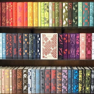 Puede incluir: Una estanter&iacute;a llena de libros de tapa dura coloridos con lomos estampados. Los libros est&aacute;n dispuestos en filas en las estanter&iacute;as. La fila superior presenta libros con lomos verdes, amarillos, naranjas y rojos. La fila del medio presenta libros con lomos azules, morados y rosas. La fila inferior presenta libros con lomos marrones, grises y azules. El t&iacute;tulo "Crimen y castigo" de Fi&oacute;dor Dostoievski es visible en el lomo de uno de los libros.