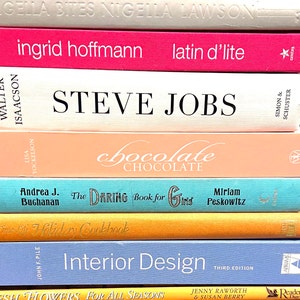 May include: A stack of books with various titles, including "Steve Jobs", "Chocolate", "The Daring Book for Girls", "Interior Design", and "Fresh Flowers for All Seasons".