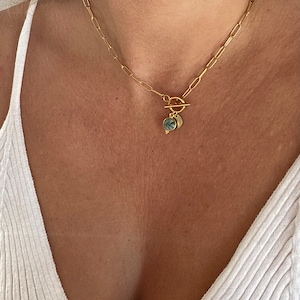 May include: A gold chain necklace with a toggle clasp and two round pendants. The pendants are made of gold and have a green and gray stone inlay.