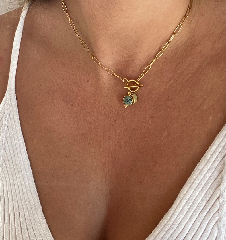May include: A gold chain necklace with a toggle clasp and two round pendants. The pendants are made of gold and have a green and gray stone inlay.