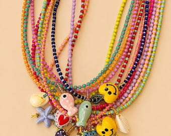 Puede incluir: Un collar de múltiples hilos con cuentas de vidrio multicolores y vibrantes. El collar está adornado con varios dijes, incluyendo caras sonrientes amarillas, peces de cerámica, estrellas de mar azules, conchas blancas y colgantes en forma de corazón.