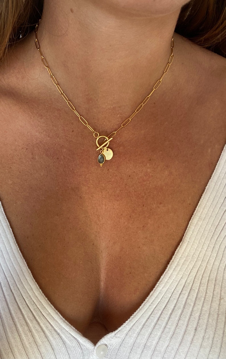 May include: A gold chain necklace with a toggle clasp and a small round pendant with a blue gemstone.