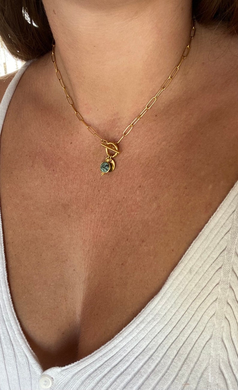 May include: A gold chain necklace with a toggle clasp and a green stone pendant.