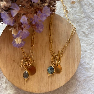 May include: Two gold necklaces with toggle clasps and round pendants. One pendant features a light blue gemstone, the other a dark green and white gemstone.