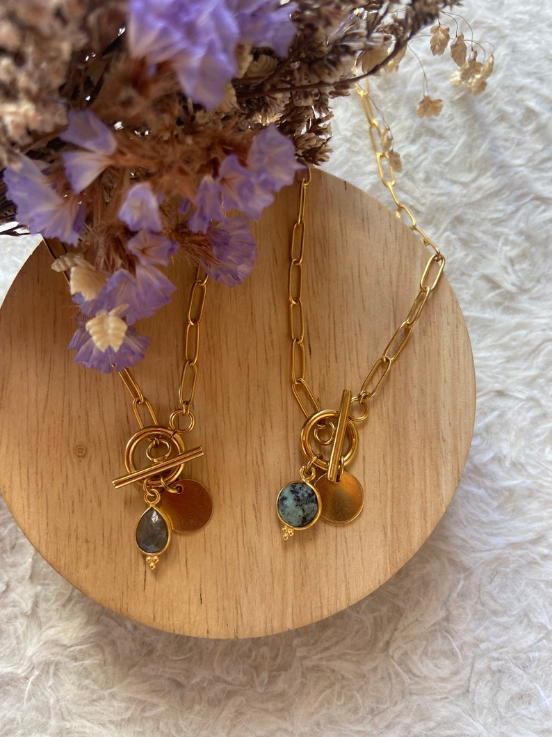May include: Two gold necklaces with toggle clasps and round pendants. One pendant features a light blue gemstone, the other a dark green and white gemstone.