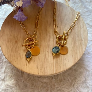 May include: Two gold necklaces with toggle clasps and stone pendants. One necklace has a green stone pendant and the other has a blue stone pendant.