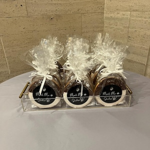 May include: Three round, black and white dipped cookies individually wrapped in clear cellophane bags with white ribbon ties. Each cookie features a circular black label with the white text "Meet Me @ Studio BK" displayed on a clear tray.