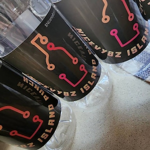 May include: Several clear plastic bottles with black labels. The labels feature a circuit board design in shades of orange and pink, along with the text "NICEVYBZ ISLAND" and "PUNCH". The bottles are partially filled.
