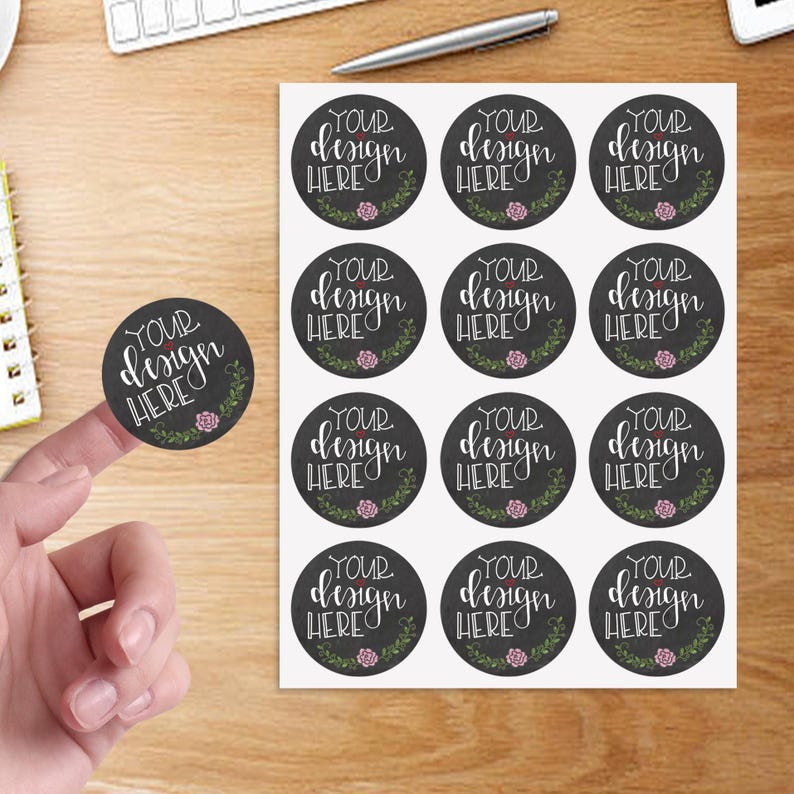 May include: A sheet of twelve circular stickers and one individual sticker featuring a dark gray background with white cursive text that reads YOUR DESIGN HERE, accented by a small pink flower and green leafy vine graphic at the bottom.