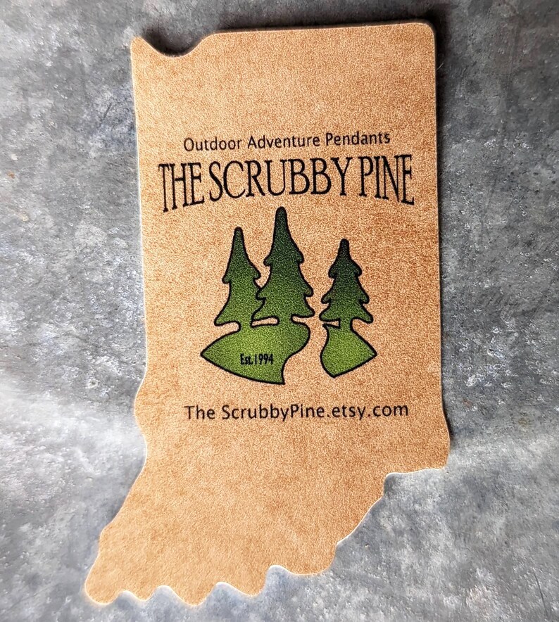 May include: A brown leather-like tag shaped like the state of Indiana with the text "Outdoor Adventure Pendants THE SCRUBBY PINE Est. 1994 The ScrubbyPine.etsy.com" printed on it. The tag features a green silhouette of three pine trees.