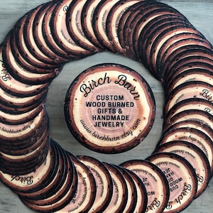 May include: Circular wooden coasters with a wood-burned design, featuring the text "Birch Barn" and "Custom Wood Burned Gifts & Handmade Jewelry." The coasters are arranged in a circular pattern, showcasing a rustic aesthetic.