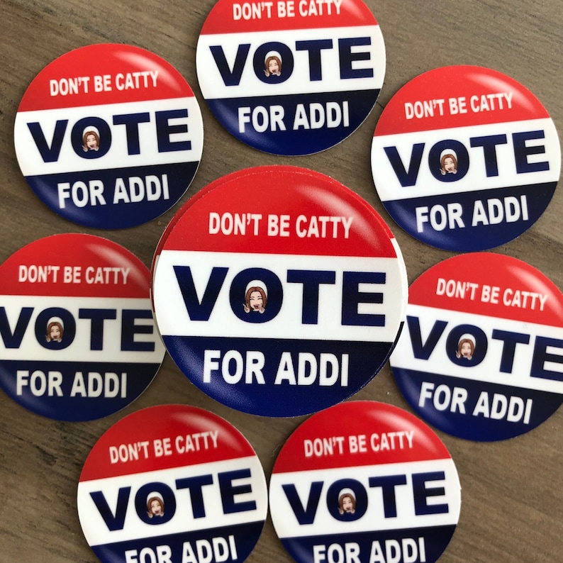 May include: A collection of round, red, white, and blue buttons. Each button has the text "DON'T BE CATTY" at the top, "VOTE" in the center, and "FOR ADDI" at the bottom. A small image of a person is in the center of the "VOTE" text.