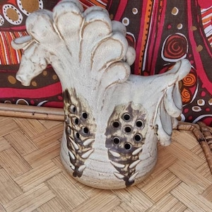 May include: A white ceramic horse figurine with brown accents and holes throughout. The figurine is sitting on a woven surface.