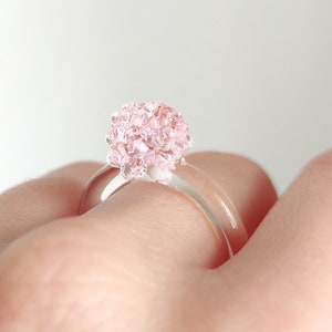 May include: A clear glass ring with a pink glass flower design.