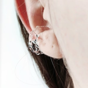 Könnte beinhalten: Ein transparenter Ohrring aus Harz mit einer einzigartigen, organischen Form. Der Ohrring wird im oberen Teil des Ohrs getragen.