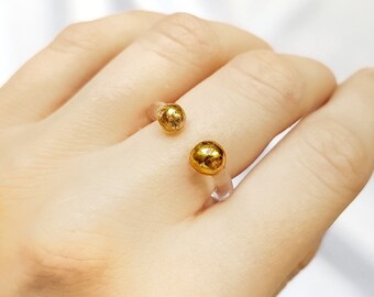 May include: A clear ring with two gold-toned spheres. The ring is open and adjustable.