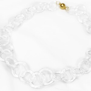 Pode incluir: Um colar de corrente de acr&iacute;lico transparente com um fecho dourado.
