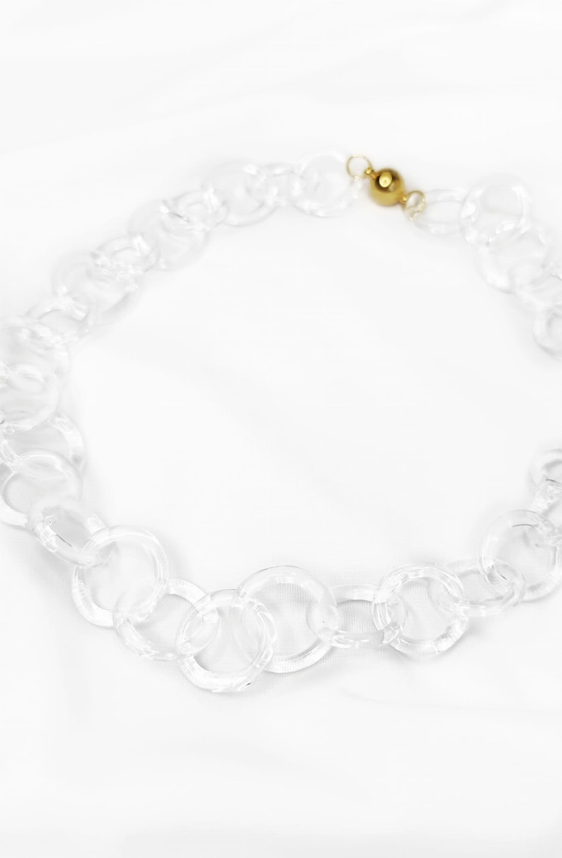 Pode incluir: Um colar de corrente de acr&iacute;lico transparente com um fecho dourado.