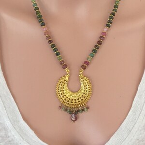 May include: A gold necklace with a crescent moon pendant and a beaded chain made of green, pink, and brown gemstones.