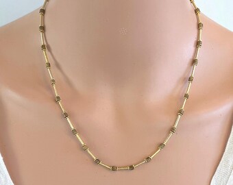 May include: A gold necklace with small, square-shaped beads. The necklace is on a mannequin's neck.
