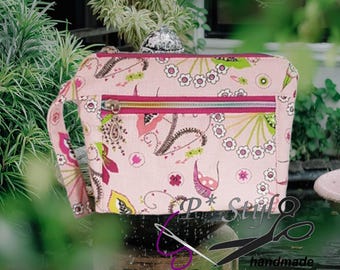Könnte beinhalten: Eine hellrosa Reißverschlusstasche mit einem bunten Blumen- und Paisleymuster in Magenta, Limettengrün und Weiß. Die rechteckige Tasche verfügt über eine Handschlaufe an der linken Seite und einen Metallreißverschluss mit dekorativem Anhänger.