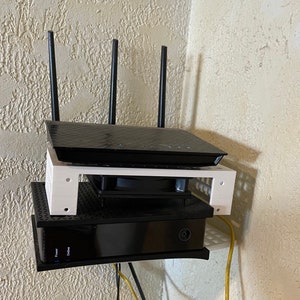 May include: A white shelf with two black electronic devices mounted on a wall. The top device has three antennas and the bottom device has a power button labeled "Power".