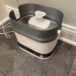 May include: A white and grey pet water fountain with a water spout. The fountain has a white base with a black trim and a grey top. The brand name "PETLIBRO" is visible on the front.