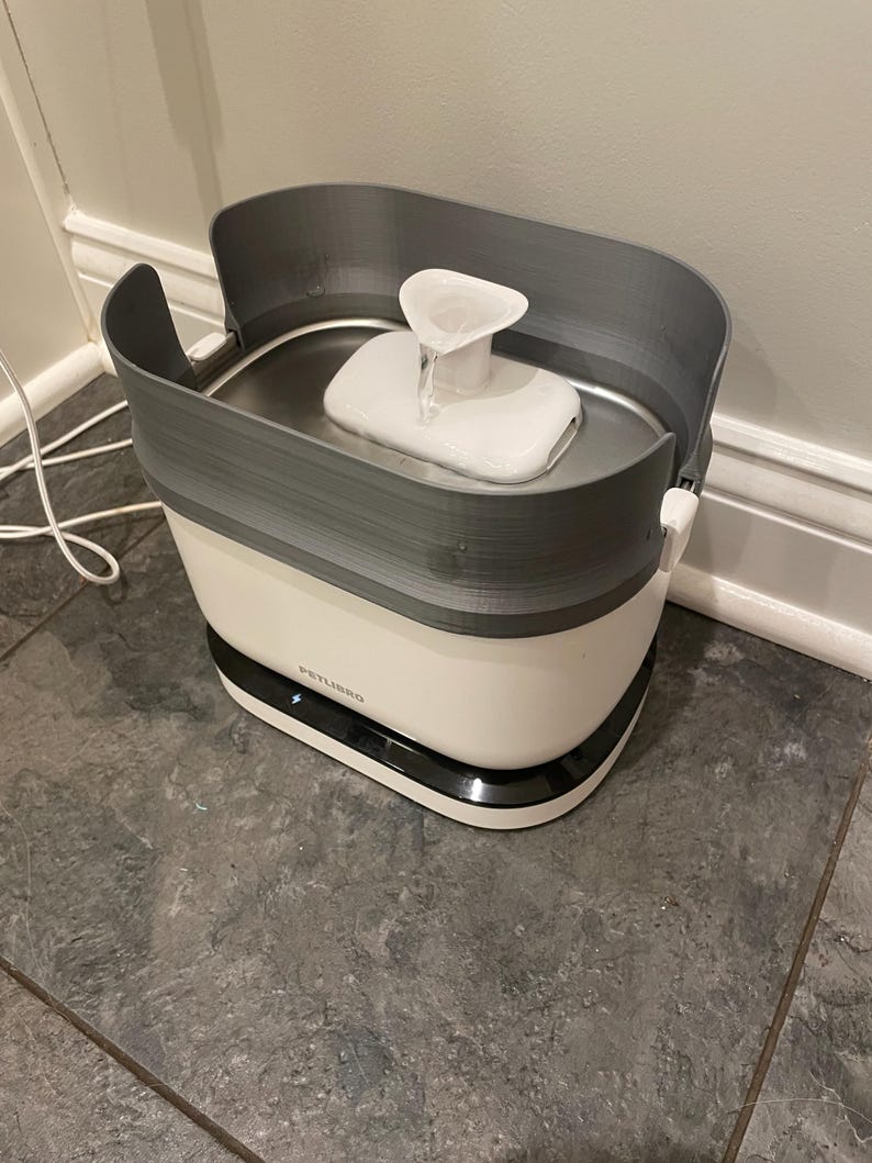May include: A white and grey pet water fountain with a water spout. The fountain has a white base with a black trim and a grey top. The brand name "PETLIBRO" is visible on the front.