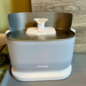 May include: A light blue PETLIBRO pet water fountain with a white base. The fountain has a water reservoir and a white, tiered water feature. The water fountain is designed for pets.
